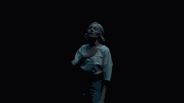 a woman in a white shirt and blue jeans is standing in a dark room