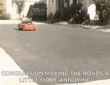 a red remote control car is driving down a street in front of a house .