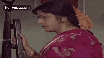 a woman in a red saree is standing in front of a mirror and looking at herself .