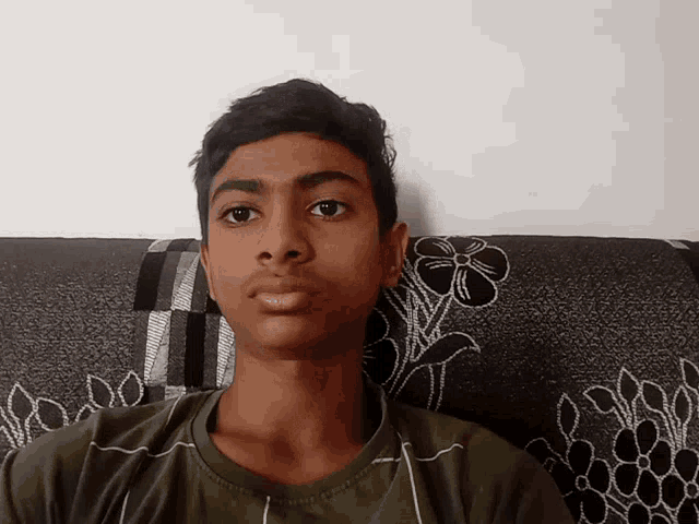 a young boy sitting on a couch with a flower pattern on the cushion