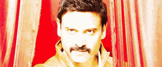 a man with a mustache is peeking out of a red curtain