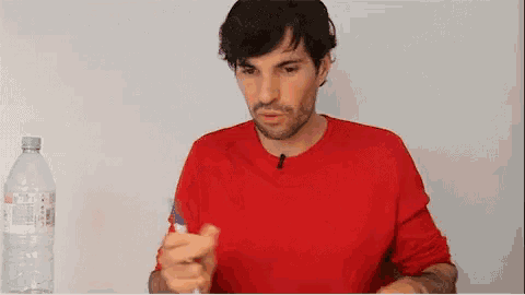 a man in a red shirt is holding a pen and a bottle of water