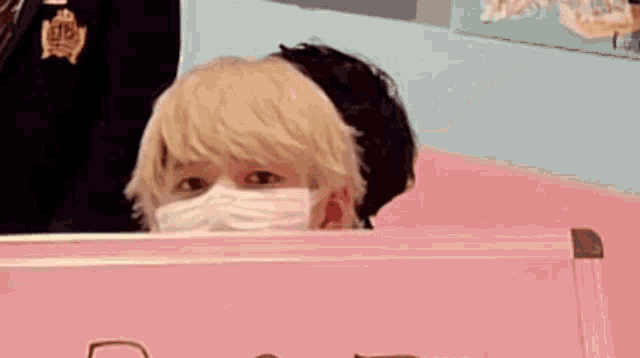 a man wearing a mask is looking at a stuffed animal behind a pink box .