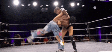 two men are wrestling in a ring and one of them is wearing a pair of jeans with graffiti on them .