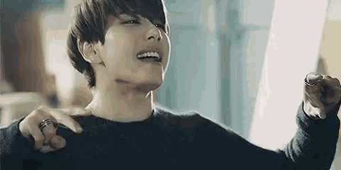 a young man wearing a black sweater and a ring on his finger is laughing .