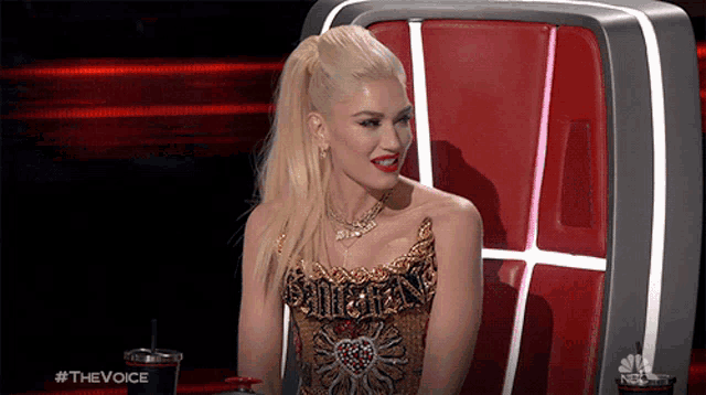 a woman is sitting in a chair with a cup of soda in front of her that says #thevoice on it