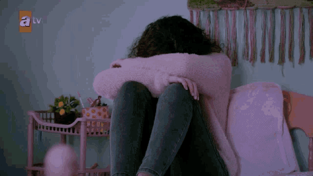 a woman sits on a bed with her head in her hands and a tv logo in the corner