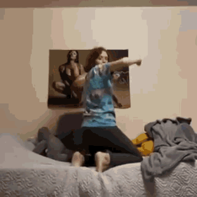 a woman is kneeling on a bed with her arms outstretched in front of a painting on the wall .