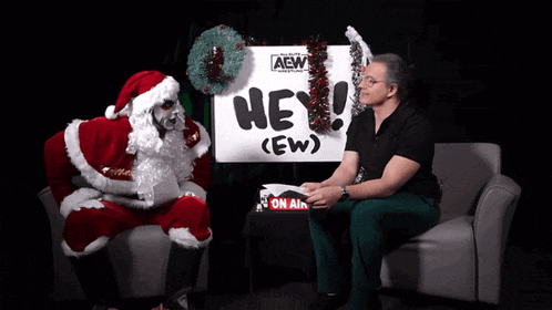 a man in a santa suit is talking to another man in front of a sign that says hey