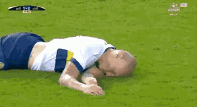 a soccer player is laying on the ground while another player kicks his foot