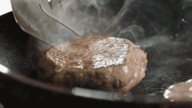 a steak is being cooked in a frying pan with smoke coming out of it