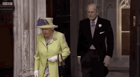 the queen and prince philip are walking out of a building . the queen is wearing a yellow coat and purple hat .