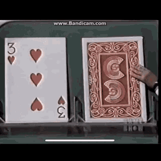 a person is holding a playing card that says three hearts on it .