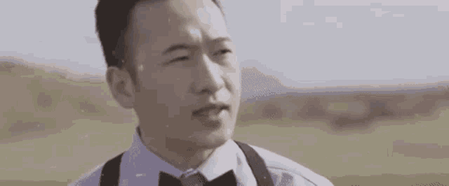 a man in a suit and tie is standing in a field with his eyes closed .