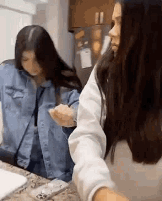 two women are standing next to each other in a kitchen . one of the women is wearing a denim jacket .