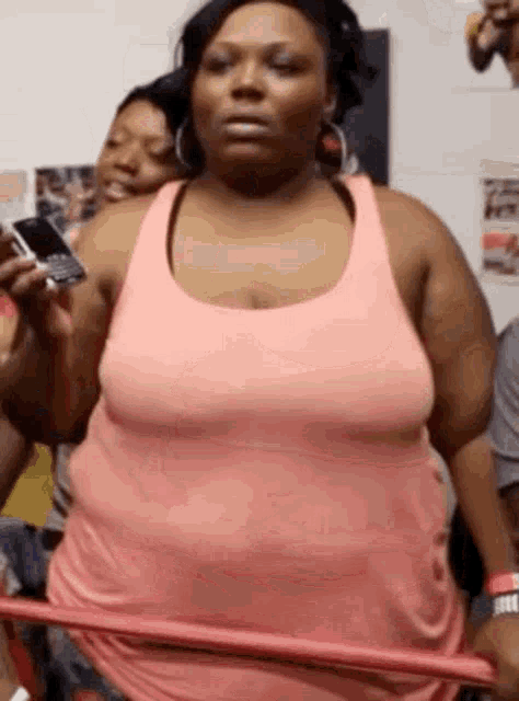 a woman in a pink tank top is holding a hula hoop in her hands .