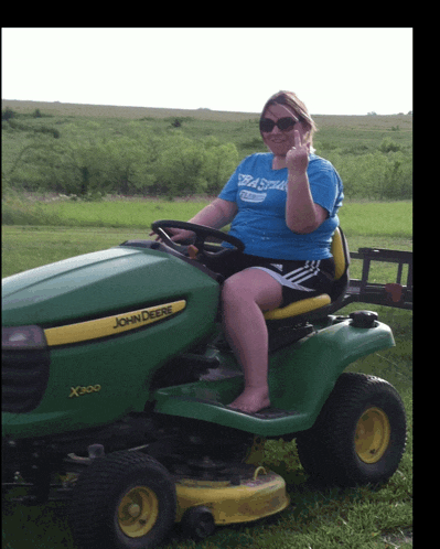 a woman in a blue shirt is sitting on a john deere x300 lawn mower