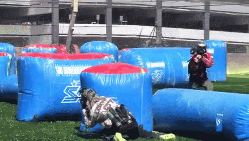 a paintball game is being played in a field with blue and red inflatable barriers