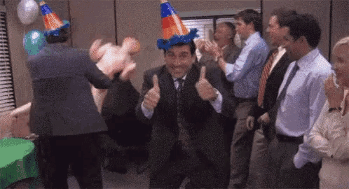 a man wearing a party hat is giving a thumbs up while dancing with a group of people .