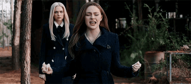two women are standing next to each other in a forest and one of them is screaming .