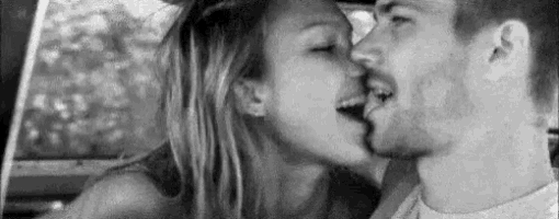 a man and a woman are kissing in a car in a black and white photo .
