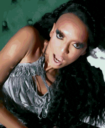 a woman with long black hair is wearing a silver top with fringe