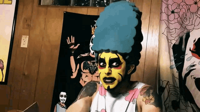 a man with a blue wig and yellow face paint is standing in front of a wall with a poster on it
