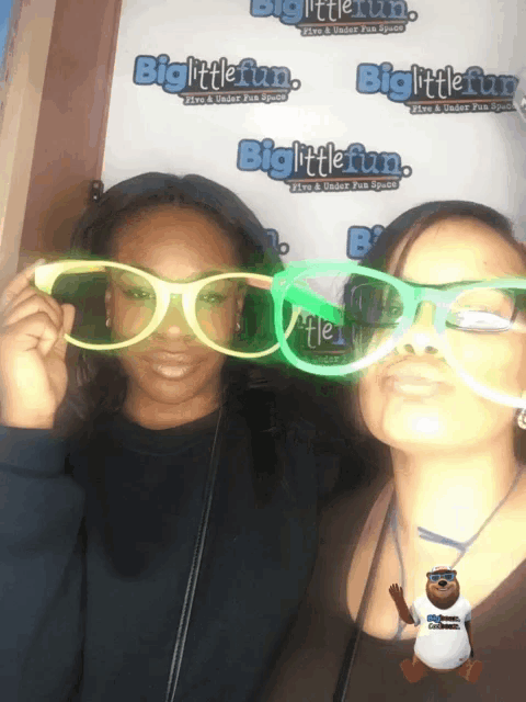 two women are posing for a picture in front of a biglittlefun sign
