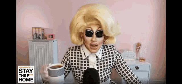 a drag queen is talking into a microphone while holding a cup of coffee