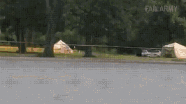 a car is driving down a road in a park with tents and trees in the background .
