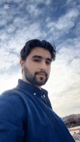 a man with a beard is taking a selfie in front of a cloudy sky .