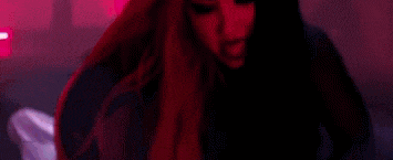 a woman with red hair is dancing in a club with a red light behind her .
