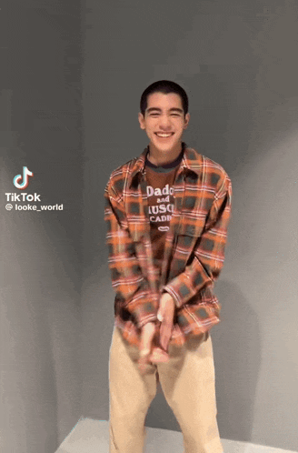 a young man wearing a plaid shirt and khaki pants is dancing and smiling .