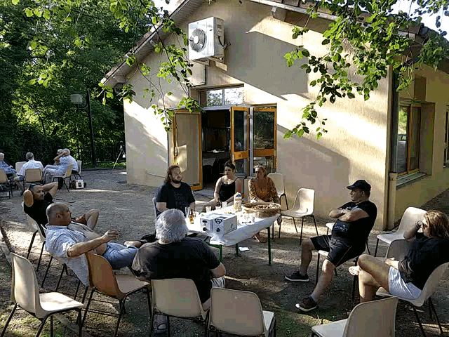 a group of people sit around a table in front of a building with an air conditioner on the side