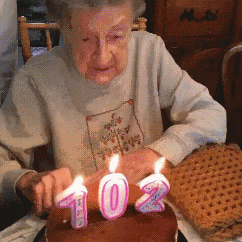 an elderly woman blows out candles on a birthday cake