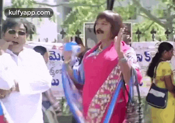 a man in a wig is standing next to a woman in a pink saree holding a broom .