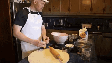 a man in an apron is preparing food in a kitchen with a bag of gold enriched flour on the counter