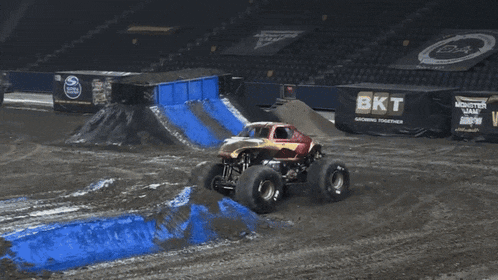 a monster truck is driving down a dirt track with a sign that says the video game in the background