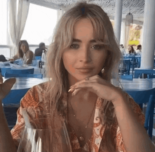 a woman is sitting at a table in a restaurant holding a glass of water .