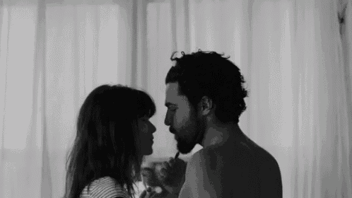 a black and white photo of a man and a woman looking into each other 's eyes .