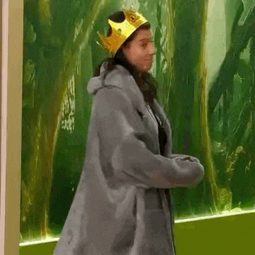 a woman wearing a fur coat and a crown is standing in front of a green wall .