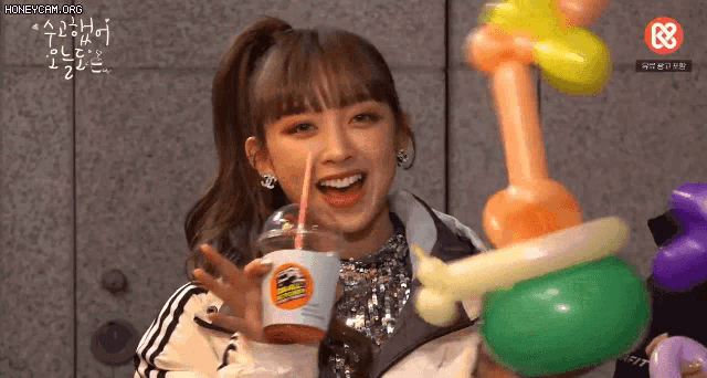 a girl is holding balloons and a cup with a straw in it .
