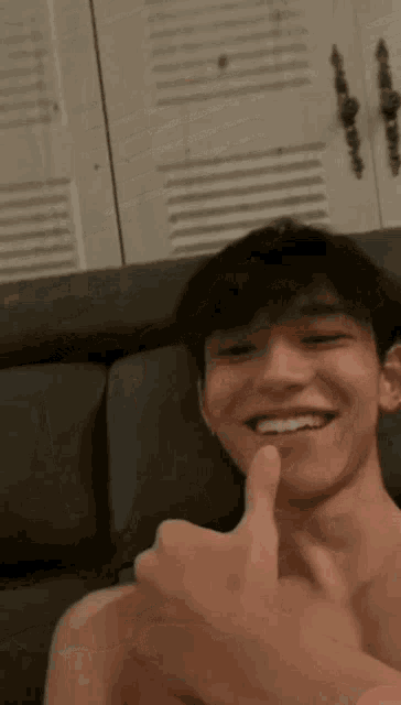 a young man without a shirt is sitting on a couch and smiling .