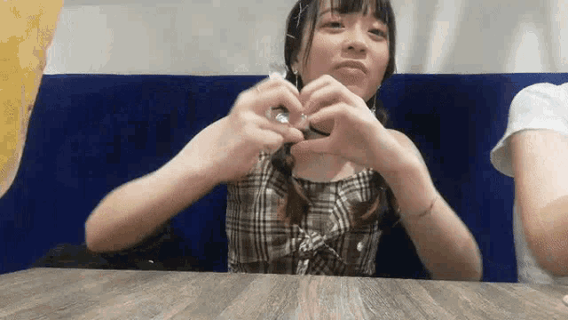 a girl is sitting at a table making a heart with her hands .