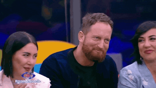 a man with a beard and two women are sitting next to each other on a television show .