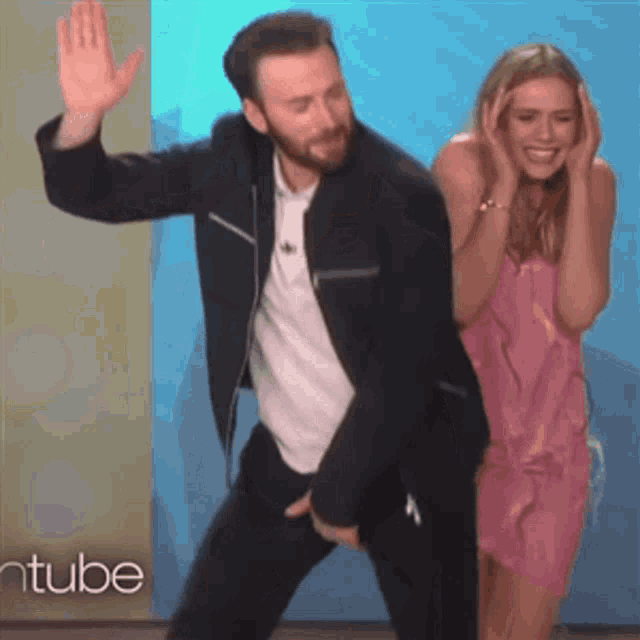 a man in a jacket is dancing with a woman in a pink dress behind him .