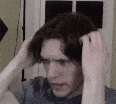 a man in a blue shirt is holding his hair in his hands