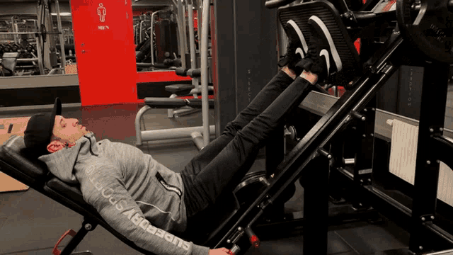 a man is laying on a bench in a gym wearing a superdry hoodie