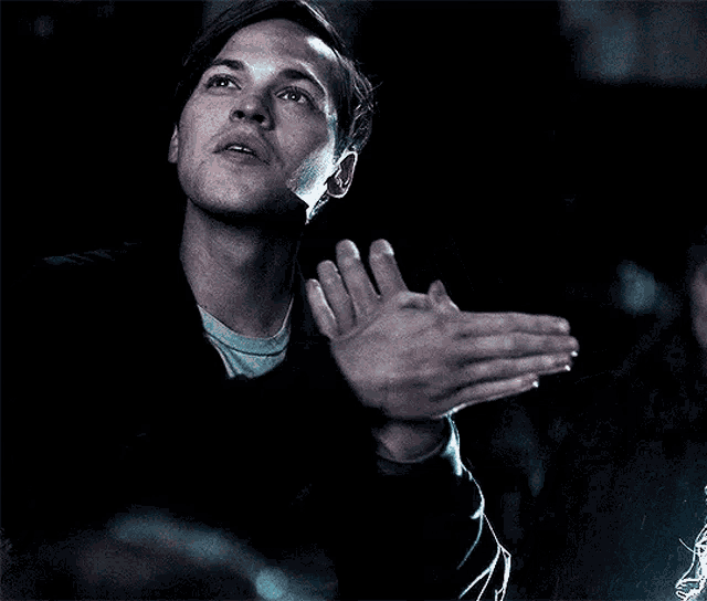 a man in a black jacket is clapping his hands in the dark