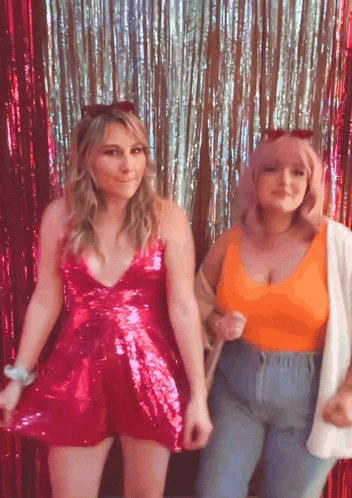 two women are posing for a picture in front of a tinsel backdrop